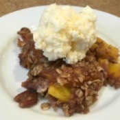 A serving of peach crumble topped with ice cream.